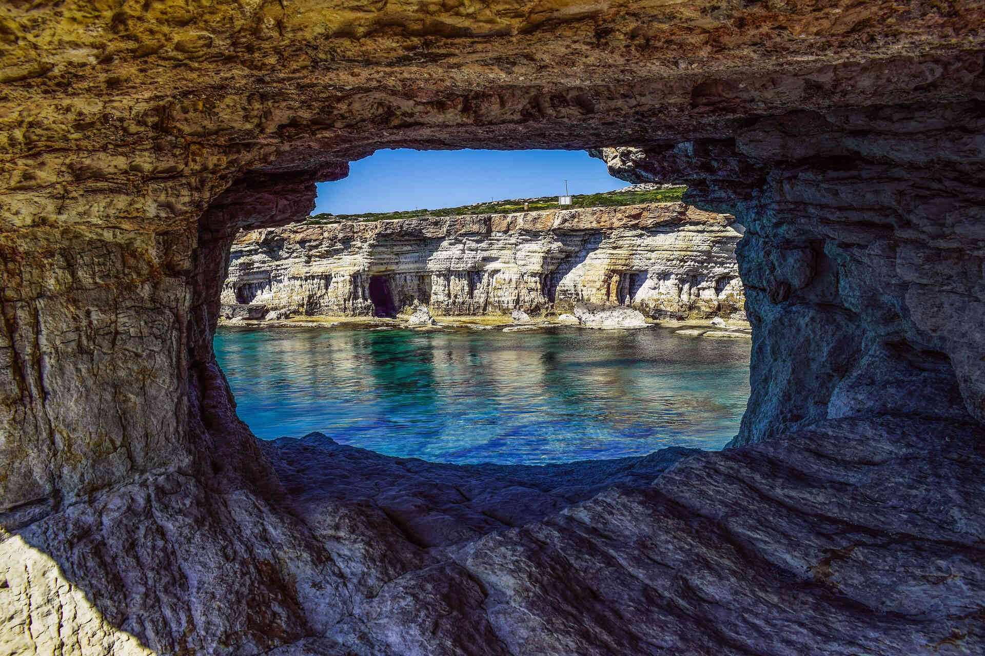 Sea caves with crystal clear turquoise water viewed through natural stone arch in Peyia