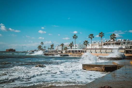 Waves breaking on the Paphos harbour seafront with palm trees and the medieval castle in the distance